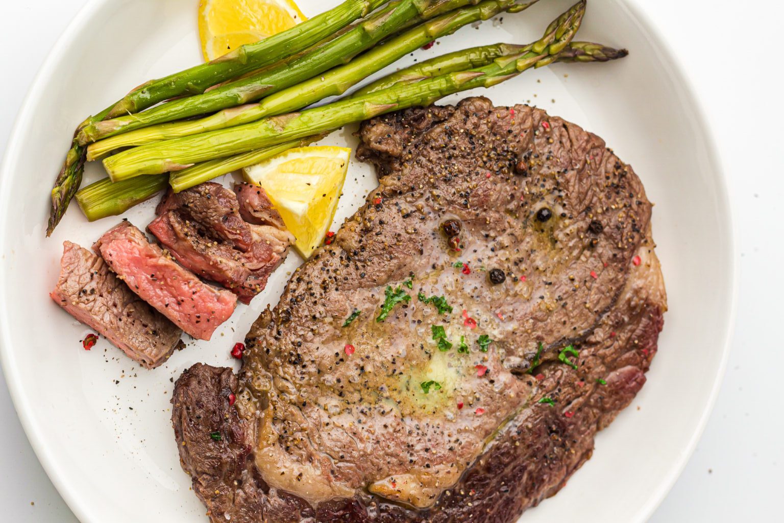 Plate with a cooked steak, sliced meat pieces, grilled asparagus, and lemon wedges.