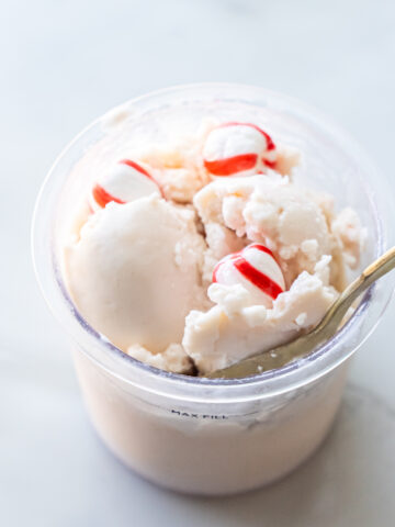 A cup of vanilla ice cream with three candy pieces on top, partially melted, with a spoon inserted on the right side.