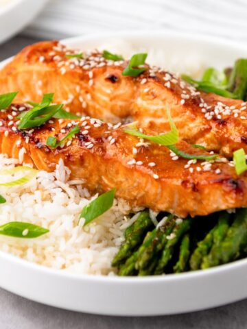 air fryer salmon topped with sesame seeds and green onions, served over white rice and asparagus on a white plate.