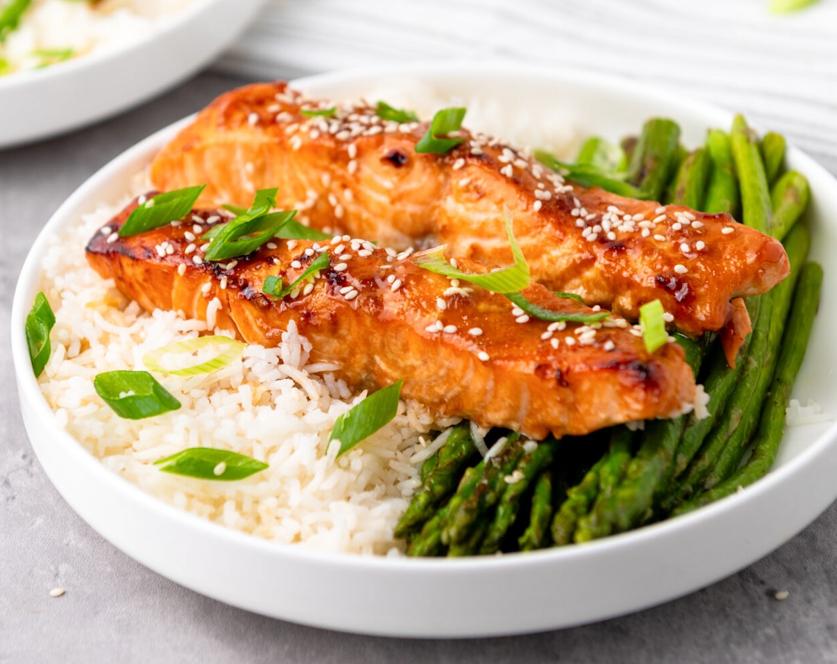air fryer salmon topped with sesame seeds and green onions, served over white rice and asparagus on a white plate.