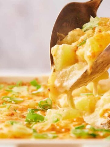 Close-up of a baked cheesy potato dish being served from a rectangular white casserole dish, garnished with chopped green onions.