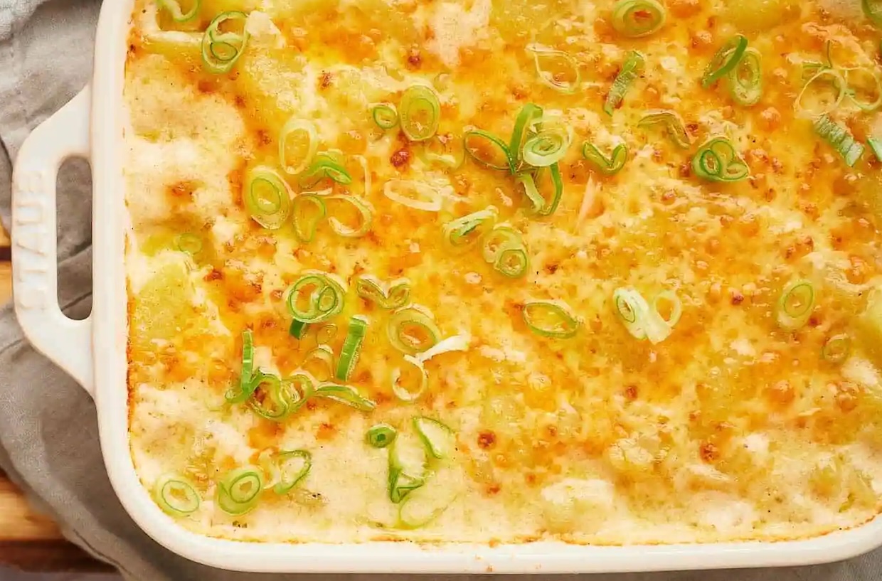 A casserole dish with golden-brown cheesy topping, garnished with sliced green onions.
