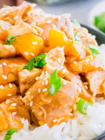 A bowl of rice topped with diced chicken, pineapple chunks, sesame seeds, and sliced green onions.