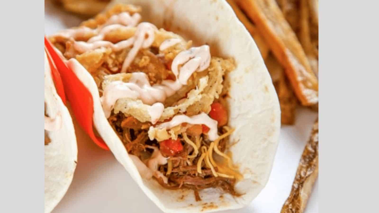 A brisket taco topped with cheese, fried onions, and a spicy sauce.