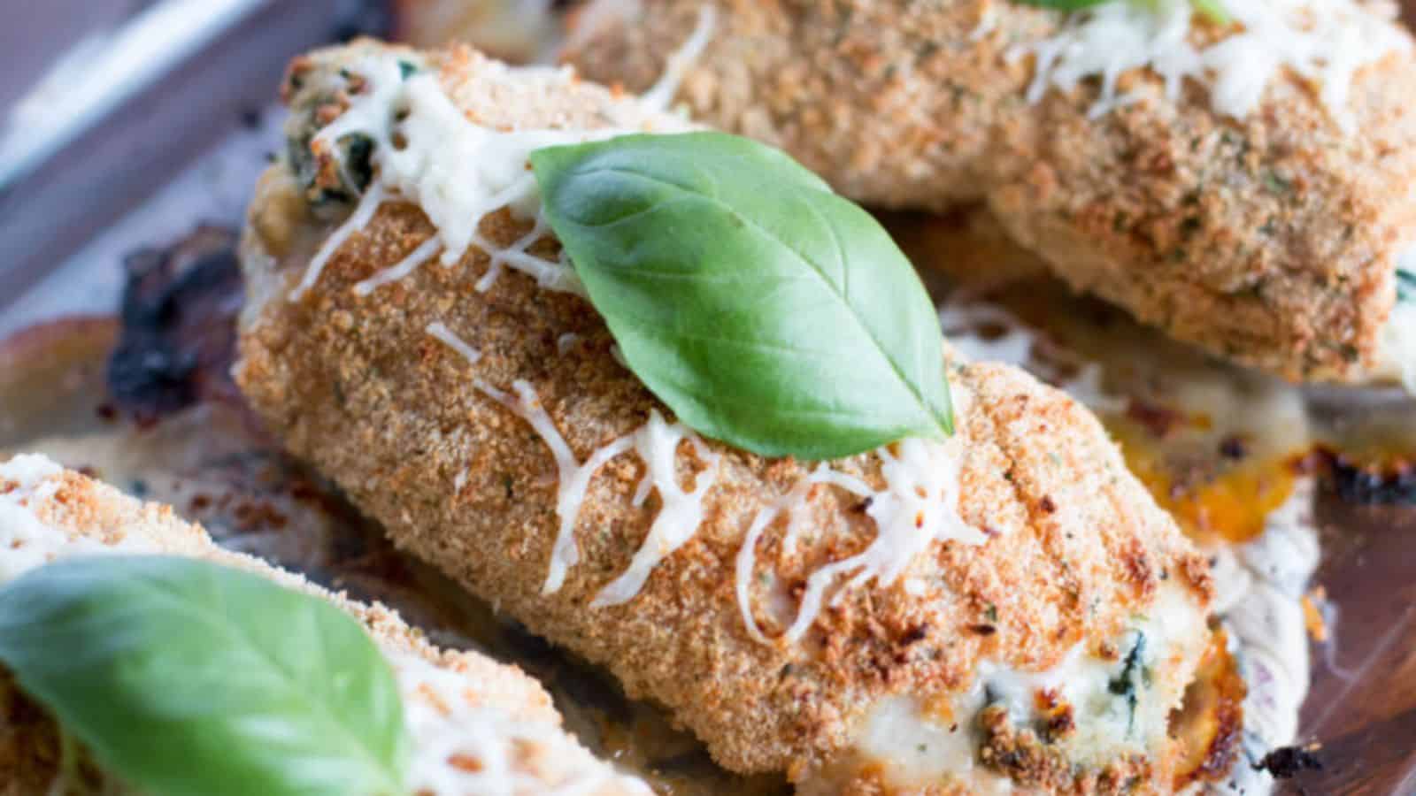 Breaded and baked stuffed chicken breast topped with melted cheese and a fresh basil leaf, served on a baking sheet—perfect for anyone seeking delicious new cheese recipes.