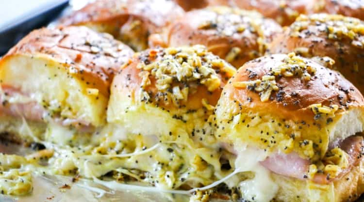 Ham and cheese sliders on baked rolls, topped with a melted butter mixture of minced onions and poppy seeds, with gooey cheese oozing out—a must-try for fans of easy cheese recipes.