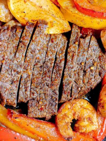 Sliced beef, shrimp, and sliced bell peppers seasoned and cooked in a pan.