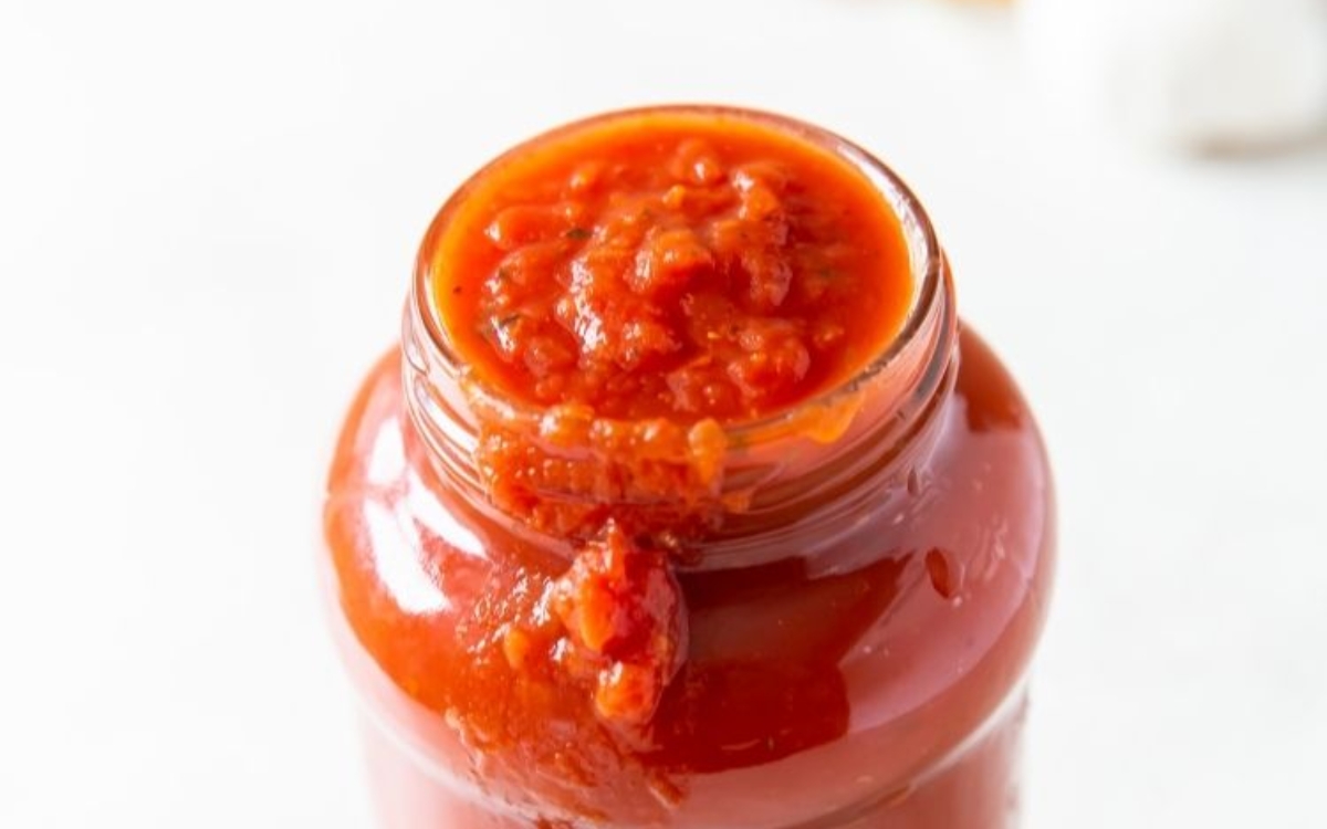 An open glass jar filled with chunky red tomato sauce, with some sauce spilling over the rim onto the side.
