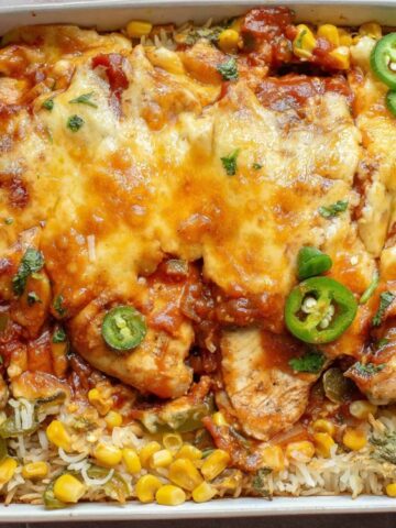 Baked casserole with melted cheese, chicken, rice, corn, and sliced jalapeños in a red baking dish—an easy chicken dinner recipe that's full of flavor.