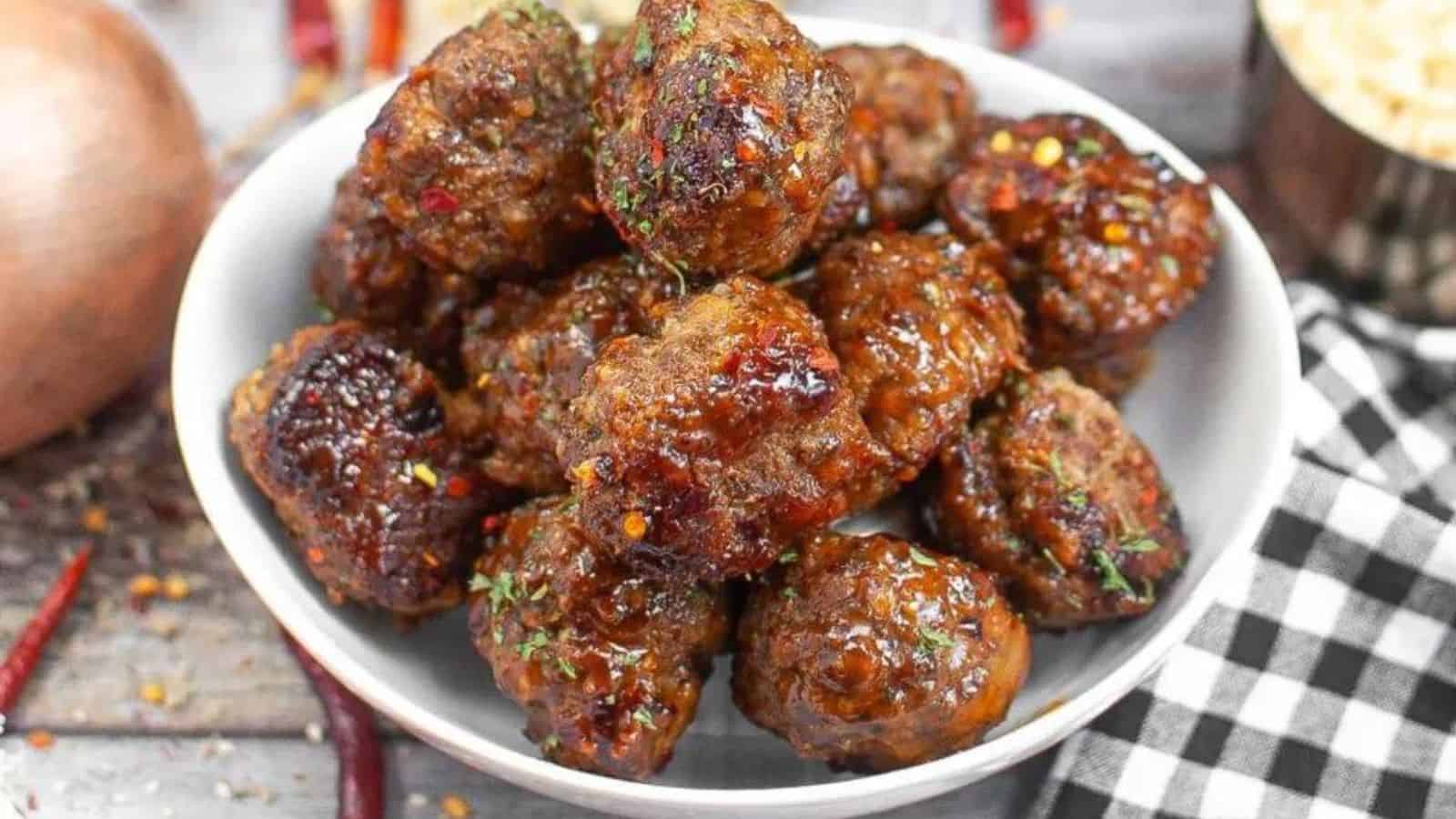 Golden meatballs with a sprinkle of herbs on a white plate, with marinara sauce.