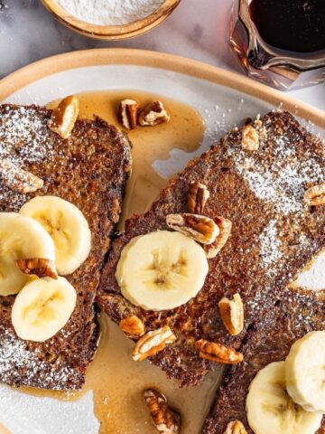 slices of banana bread in a oval plate garnish with slices of banana and a walnut