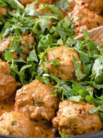 Coconut Curry Thai Turkey Meatballs scooped with wooden spoon and top with leafy greens.