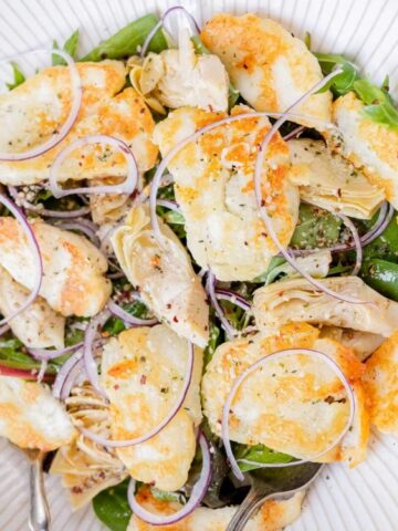 green leaves ,artichoke hearts, red onion, and dressing in a bowl