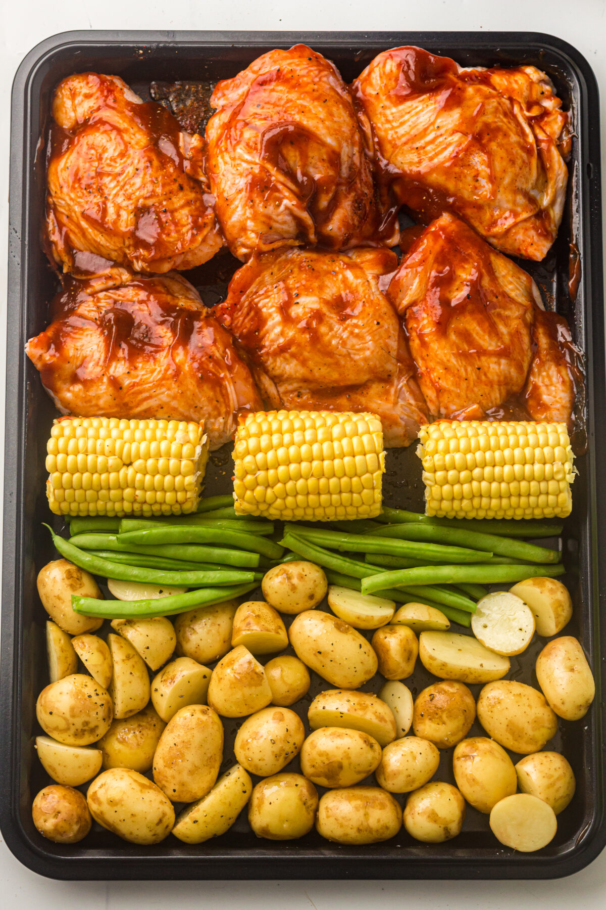 sheet pan with chicken thighs, corn, green beans and potatoes.