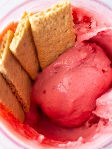 Cherry Cheesecake Ice Cream in a cup with 4 pieces of biscuit.