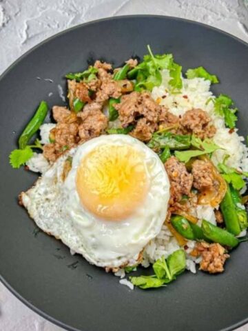 Sizzling Thai Pork and green beans with sunny side up egg and a chopsticks on the side