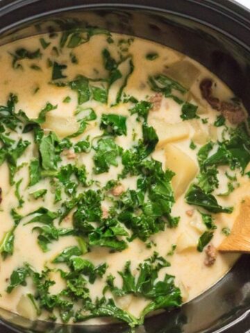 sausage kale potato soup garnish with green leaves in a pot.