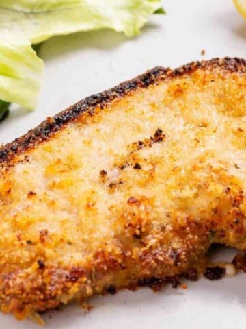 breaded pork chop in a plate with beans, lettuce and a lemon on the side