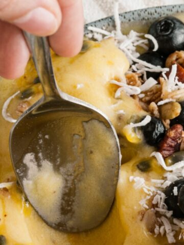 mango banana smoothie topped with blueberries, pasion fruit seeds, granola and shredded coconut on a bowl