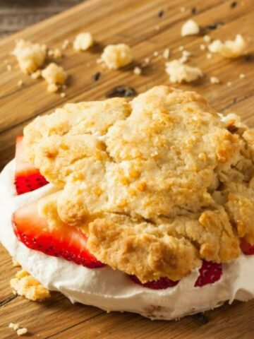 Mini Strawberry Shortcake on top of the chopping board with fresh one strawberry and crumbs on the side.