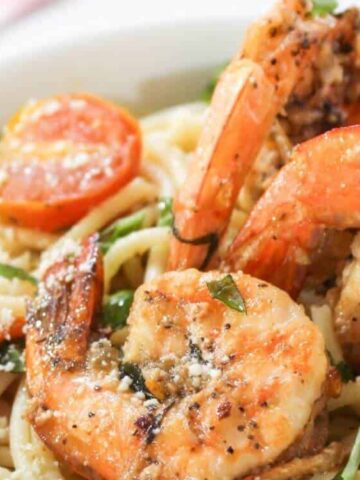 tomato past topped with shrimp and a lemon in a bowl.