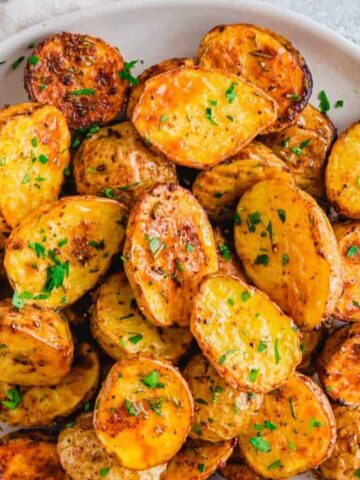 roasted baby potatoes garnished with parsley on a plate with a a serving spoon