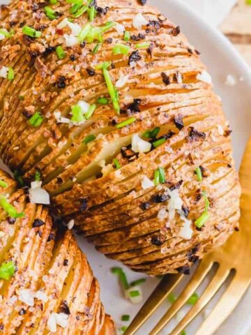 Air Fryer Hasselback Potatoes on a plate garnished with garlic and chives with fork on the side