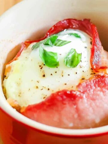 inside the red ramekin , bacon is wrapped with egg and topped with slice basil