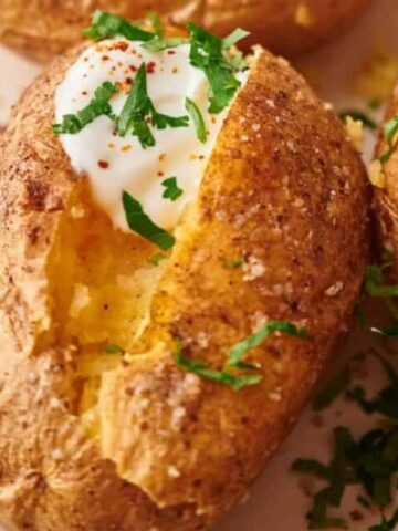 baked potato slice in the middle top with white sauce and garnish with chopped basil on a plate
