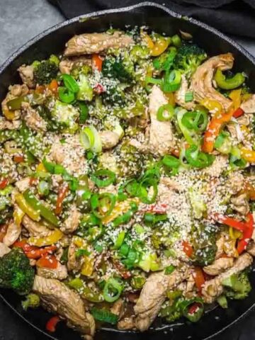 stir fry chicken with broccoli , colorful bell peppers, green onion and sprinkled with sesame seeds in a pan
