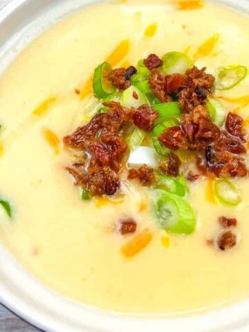 light yellow soup in a bowl topped with garlic, c=bacon and chopped green onions