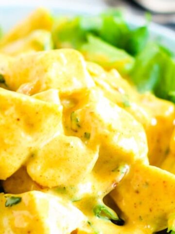lettuce top with potato coated in yellow creamy dressing on a plate