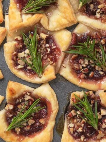 tart crust filled with cranberry sauce sprinkled with pecan and garnish with rosemary on a cooling rack.