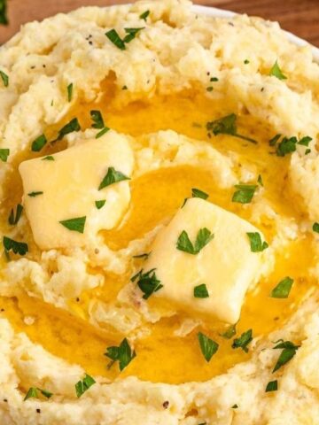 Garlic Mashed Potatoes topped with butter and shopped parsley in a bowl