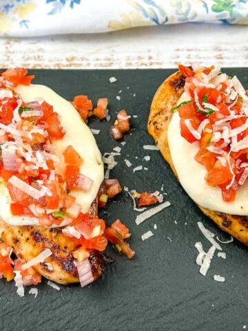 grilled chicken breast topped with cheese, tomato, onion, garnish with basil leaves
