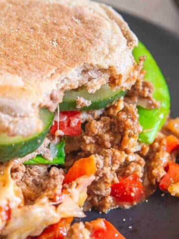 burger buns stuffed with ground beef, slices of cucumber, red bell pepper and cheese on a plate