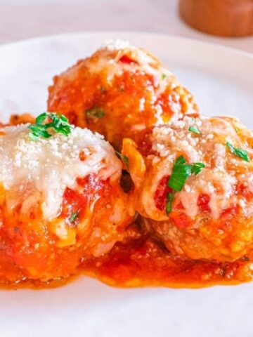 meatball sprinkled with parmesan cheese and basil leaves in a saucer