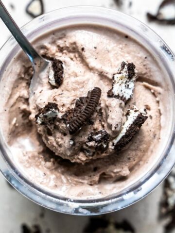 cookies n cream ice cream in a cup top with crashed cookies with a spoon and with a background of crashed cookies