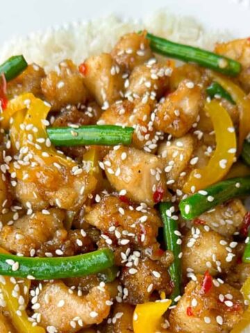 chicken, yellow bell pepper, beans in a plate topped with sesame seeds with chopsticks on the side