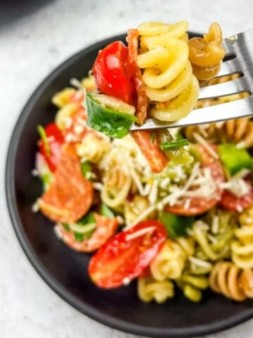 rotini pasta, Pepperoni, cheese, Grape tomatoes, Green bell pepper, onion, and Parsley in a black bowl