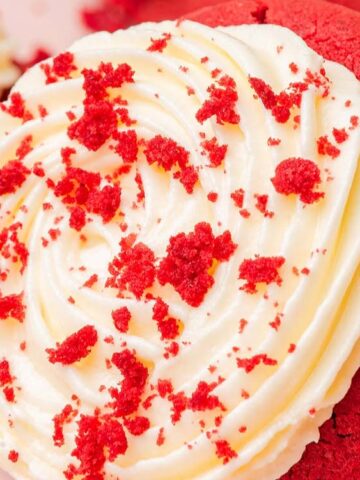 red velvet cookie with white cream and sprinkled red velvet crumbs on top of it.