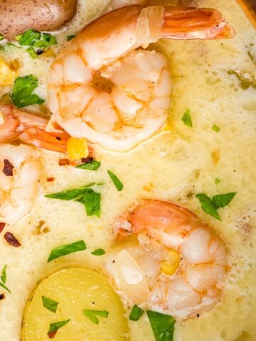 creamy white soup with shrimp and potato with shopped parsley in a pot