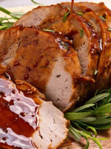 cut pork loin poured with brown sauce in a wooden chopping board garnish with fresh rosemary