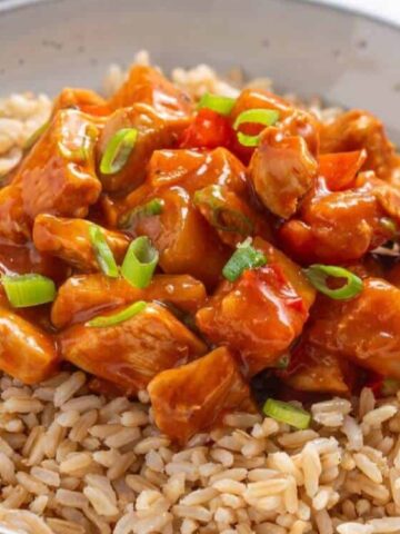 rice top with brown saucy chicken, pineapple chunks and red bell pepper garnished with green onion leaves in a bowl