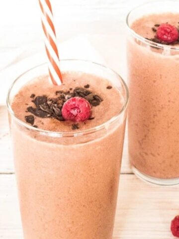 two glasses of chocolate raspberry smoothie topped with grated chocolate and raspberry fruit with straw