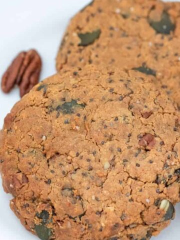 brown cookies with chopped pecan and pumpkin seeds on a plate garnished with pecan and cinnamon stick on the side