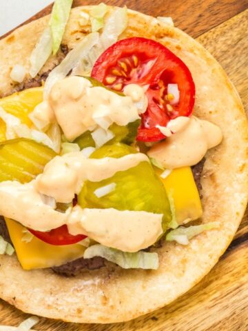 pita wrap with ground beef, pickles, white onion, cheese and white sauce on a wooden chopping board