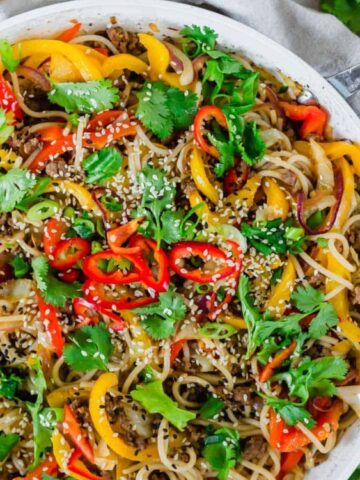 udon noodle stir fry in a white skillet garnished with sesame seeds and cilantro with chopsticks on the side