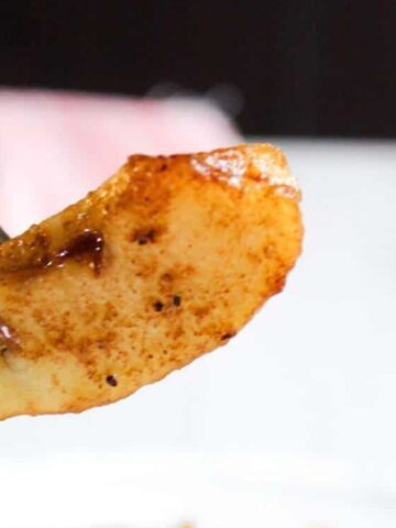 A close-up of a fork holding a slice of cooked apple dusted with cinnamon.