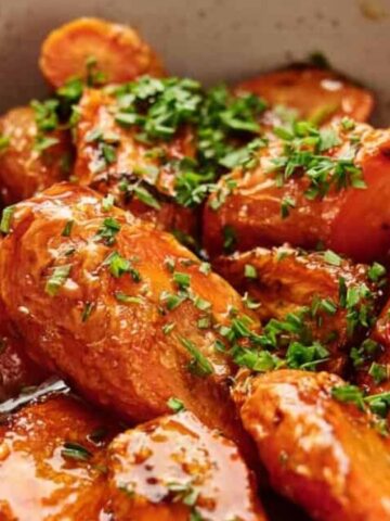 A close-up of roasted carrots topped with chopped fresh herbs, served in a shallow bowl.
